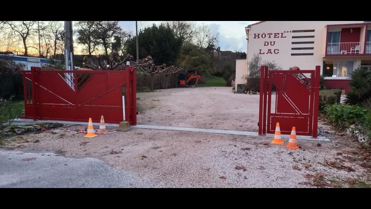 Portail coulissant et portillon rouges à l'entrée de l'Hôtel du Lac à Boussens