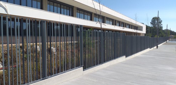 Clôture à barreaudage vertical anthracite sur muret, le long d'un bâtiment contemporain