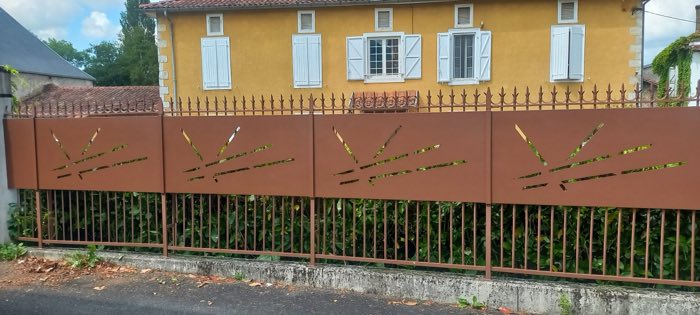 Clôture en fer forgé brun à panneaux occultants ajourés de fentes, surmontés de pointes de lance