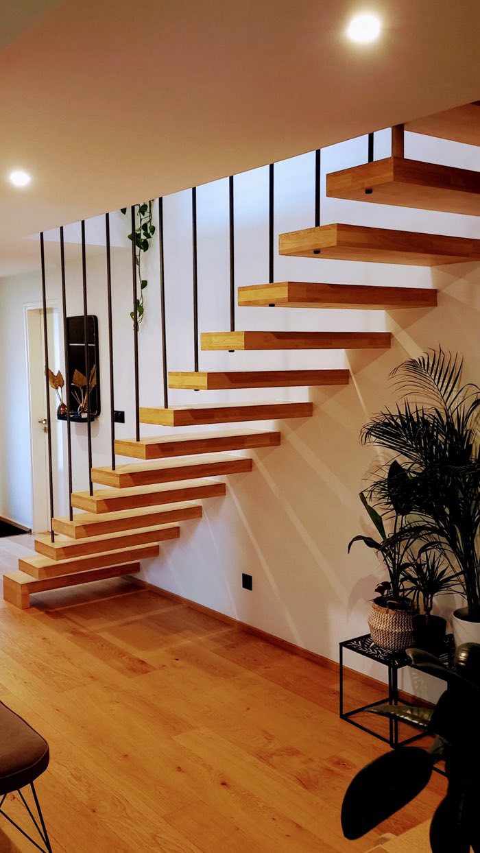 Escalier droit suspendu à marches de chêne massif, sans limon apparent, garde-corps à tiges verticales noires, dans un séjour