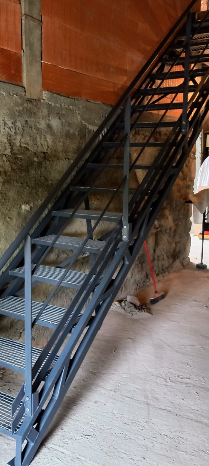 Escalier droit gris anthracite à marches caillebotis et structure en treillis, desservant un plancher bois dans une dépendance