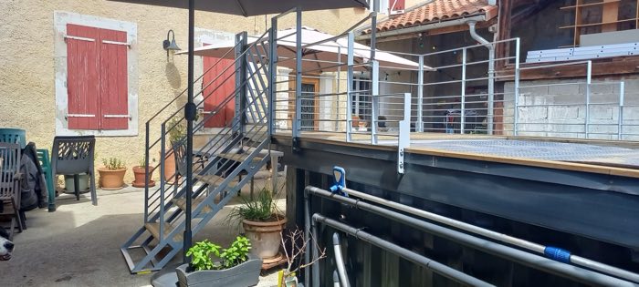 Escalier extérieur galvanisé desservant une terrasse, garde-corps à lisses horizontales, dans une cour de maison