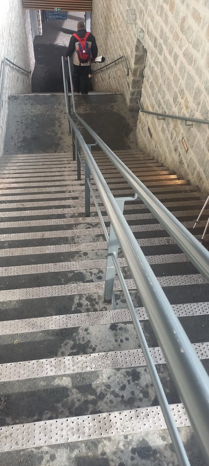 Main courante et garde-corps métalliques accompagnant un escalier en pierre, dans un passage public