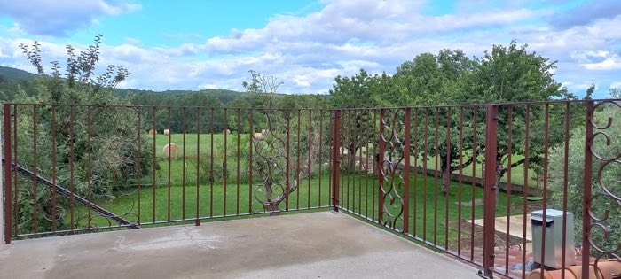 Garde-corps de terrasse en fer forgé patiné, à barreaudage et panneaux de volutes, ouvrant sur la campagne