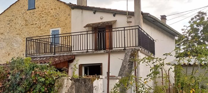 Garde-corps de balcon noir à barreaudage vertical et volutes, sur une maison de village