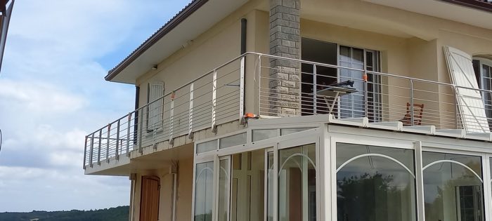 Garde-corps blanc à lisses horizontales bordant une terrasse à l'étage, au-dessus d'une véranda