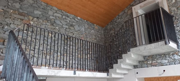 Garde-corps à barreaudage vertical accompagnant un escalier en béton, dans une grange en pierre rénovée