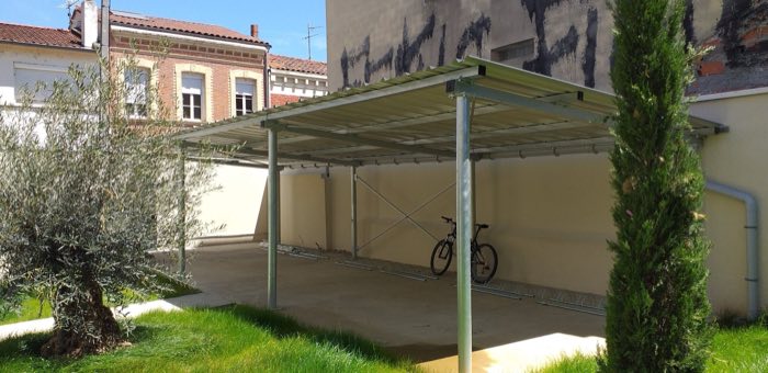 Abri à vélos en acier galvanisé à toiture monopente, implanté dans un jardin