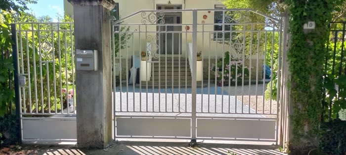 Portail battant blanc à barreaudage fin et volutes en fer forgé, avec portillon assorti, ouvrant sur un perron